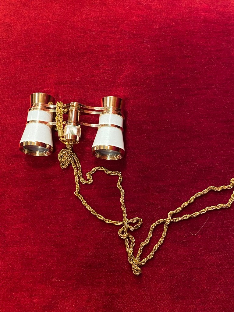 Binoculars sitting atop of a red velvet chair.